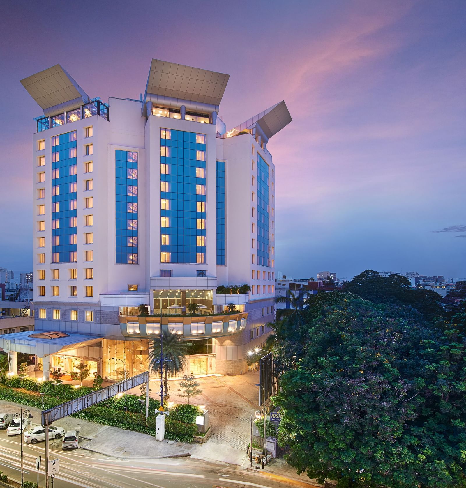 An image of a facade surrounded by trees, with cars parked in the front yard at Accord Hotels and Resorts, one of the top 5-star hotels in Chennai.